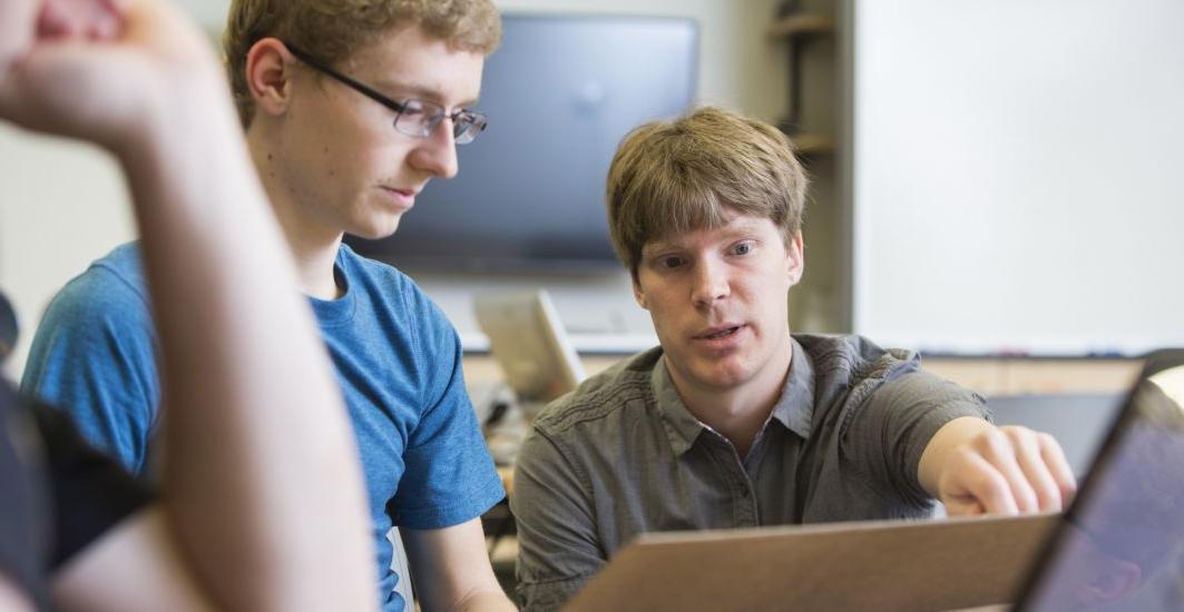 教授. Brant Carlson assists a physics major student during a physics class.